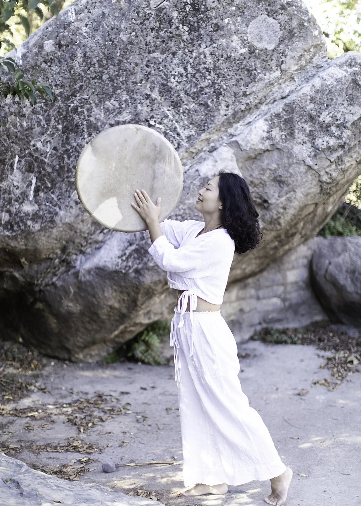 Yolanda playing an ocean drum beside a limestone boulder